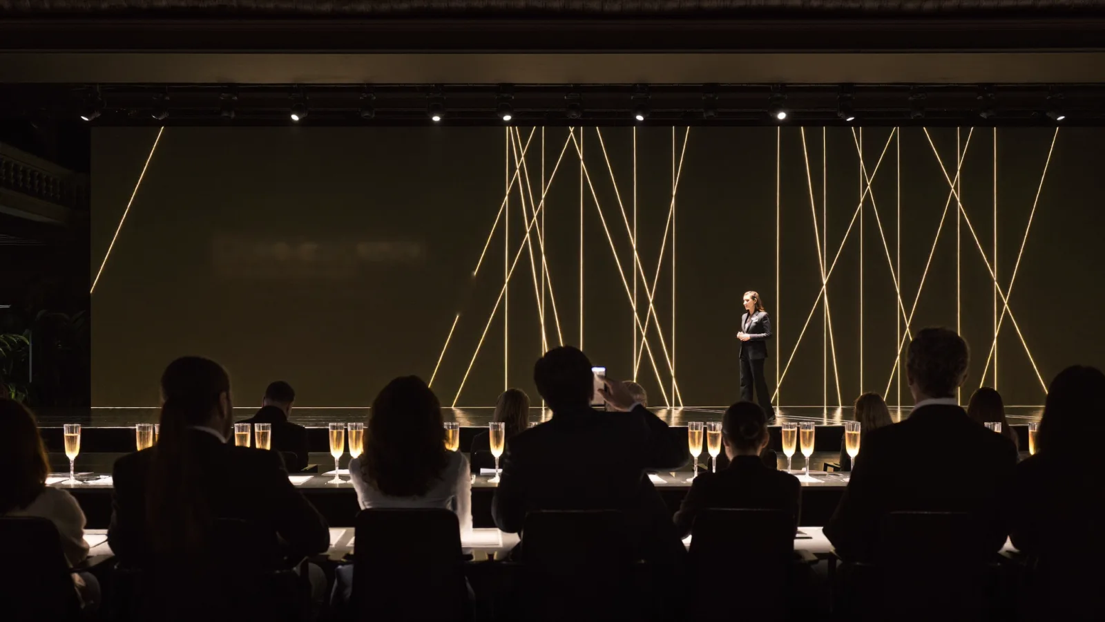 Audience watching a presenter on a stage lit with warm light lines