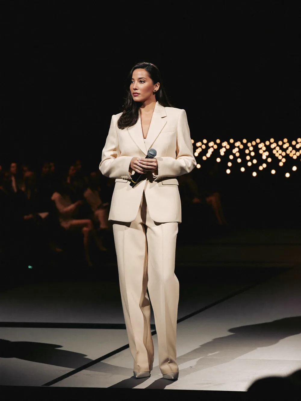 Speaker in an ivory suit on a dark conference stage
